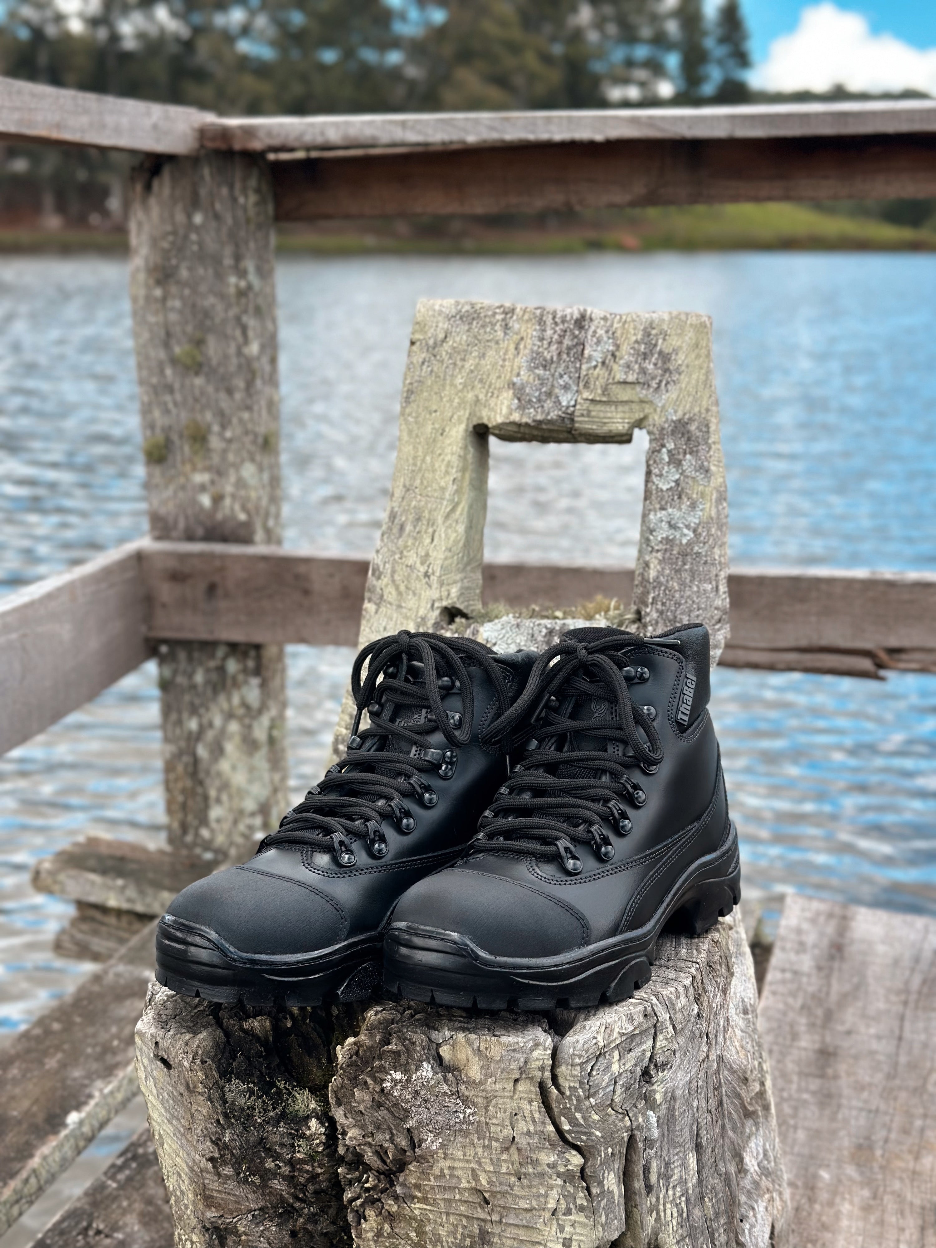 Botas impermeáveis masculinas pretas em um banco de madeira perto de um lago.