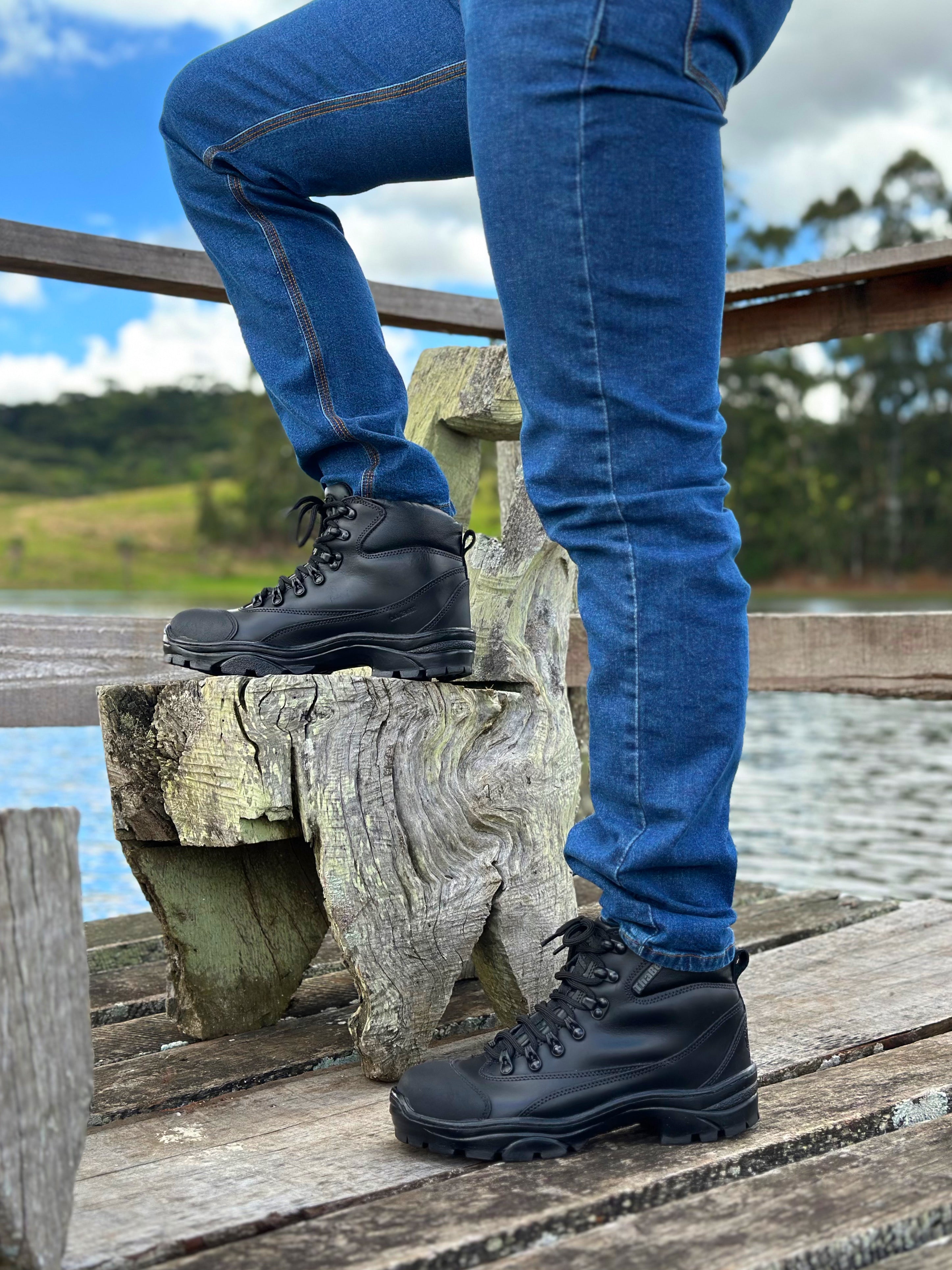 Homem usando botas coturno masculinas em um pier perto da água.