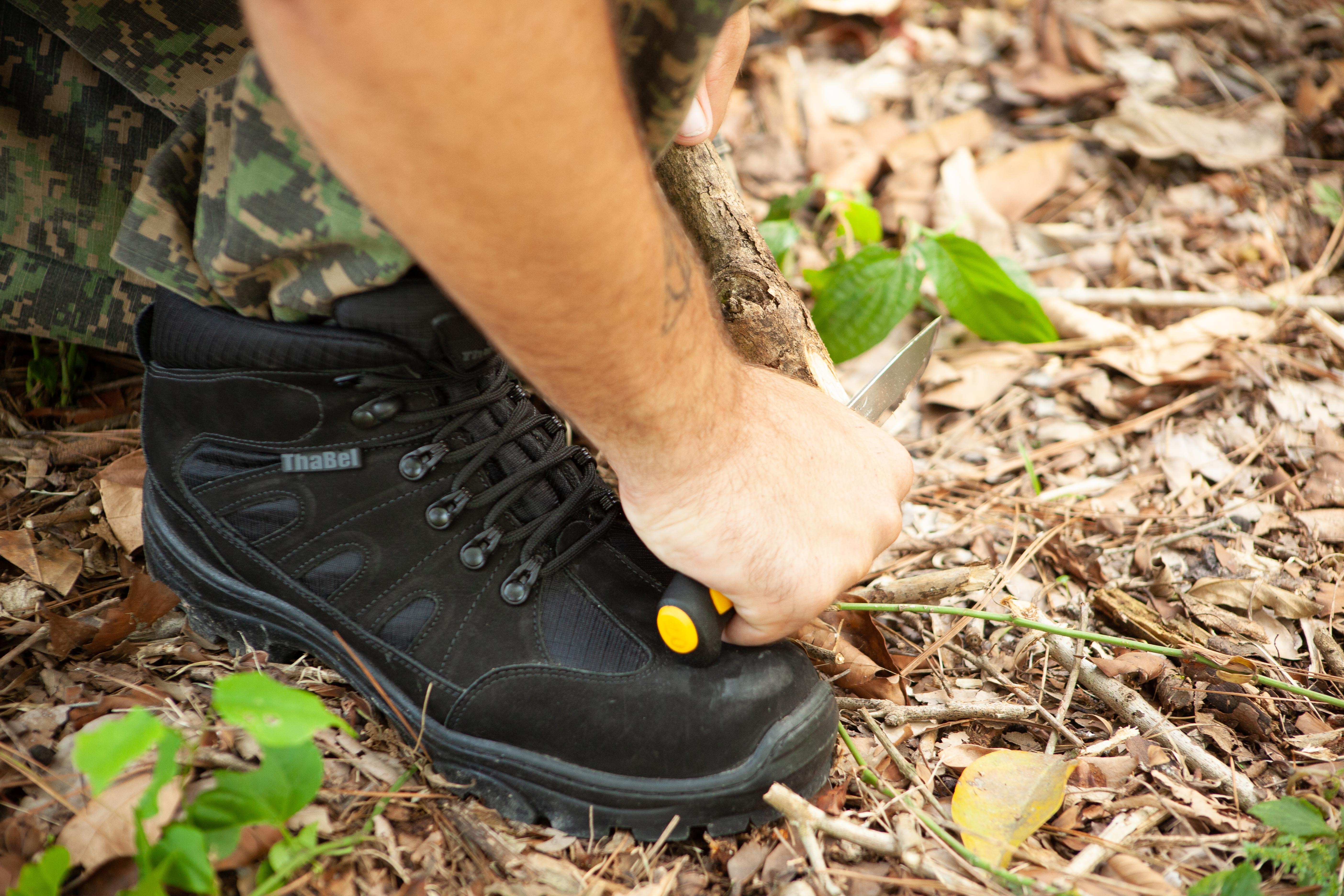 bota de segurança para aventureiros em ação, cortando um galho na floresta com foco na bota
