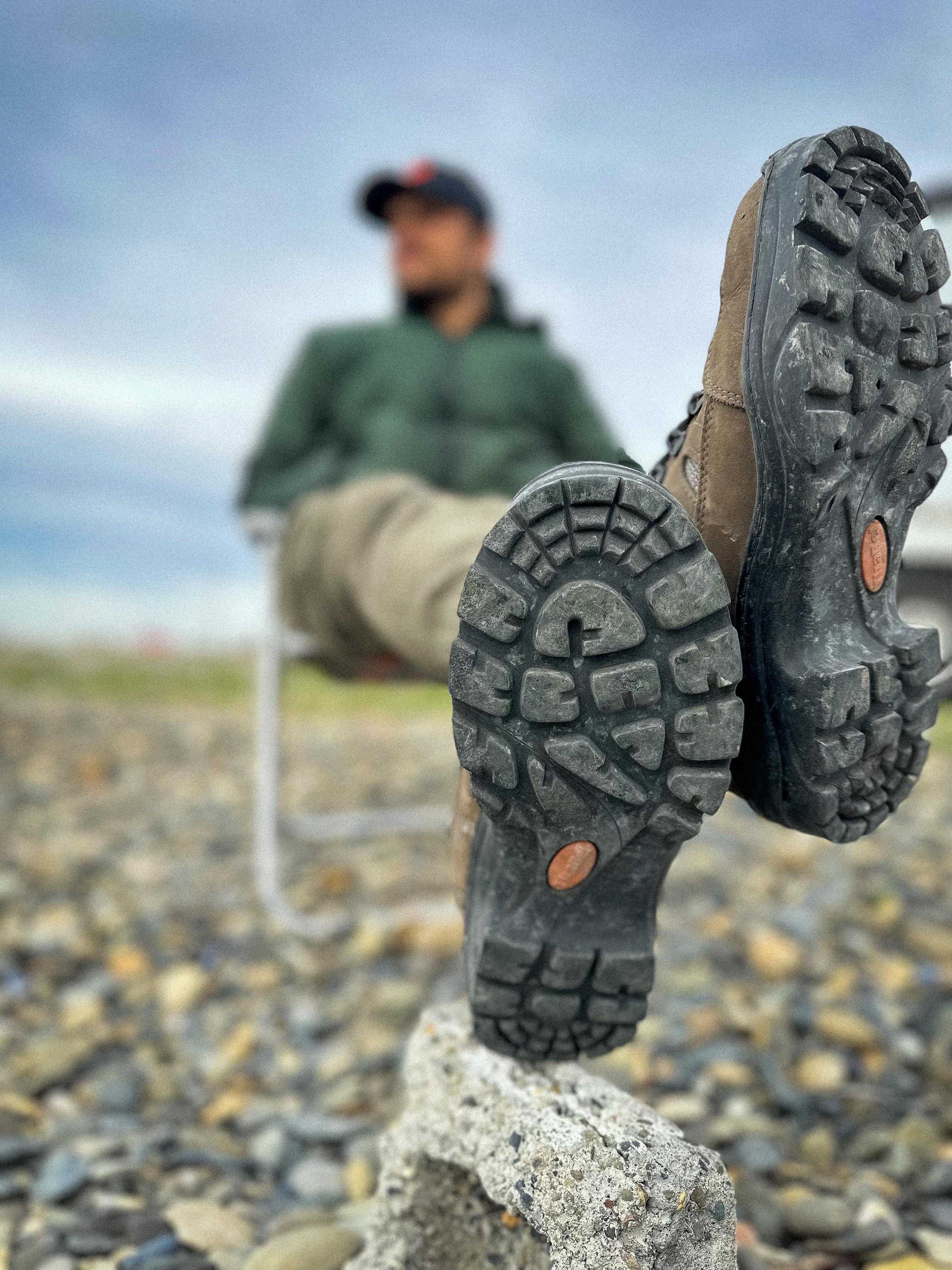 Homem relaxando em uma cadeira com botas coturno estilosas em um ambiente externo.
